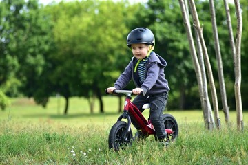 Young toddler boy riding a balance bike on a park grass. Child wearing helmet and sporty outfit enjoys outdoor fun and physical activity on a sunny day.