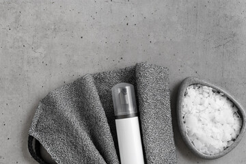 Wellness and self-care accessories, natural organic salt for bath, cosmetic bottle, exfoliating body washcloth on grey background. Home relaxation spa product, top view, copyspace, black white