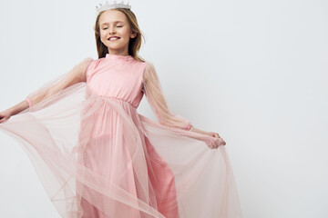 Joyful young girl in a pink dress with flowing tulle, smiling gracefully against a light...