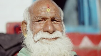 Portrait of senior Indian man with long white beard and intense eyes looking into camera lens, cultural expression, 4k video - Powered by Adobe