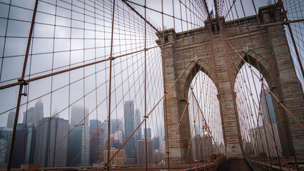 Fototapeta premium Brooklyn Bridge, the cable-stayed suspension bridge in New York City with view of Manhattan Skyline and Buildings on a foggy rainy summer morning over the East River in USA