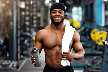 Rest after workout. Happy african american bodybuilder holding water or protein and towel at gym,...