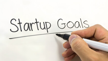 Hand writing startup goals on a whiteboard with a marker underlining the words isolated on white background