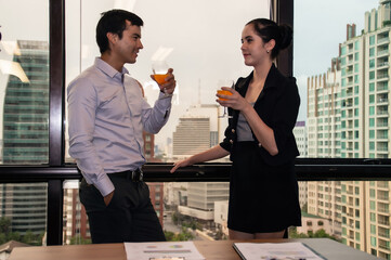 Two professionals enjoy cocktails while discussing ideas in a modern office overlooking the city skyline.