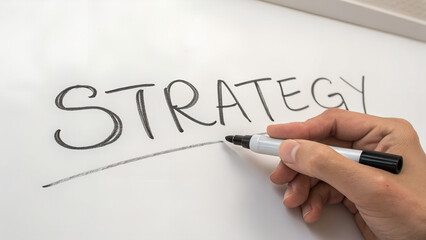 Hand writing the word strategy on a whiteboard with a marker to illustrate business planning and goal setting