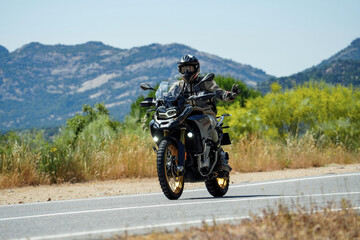 Fototapeta premium Motorcyclist waving while riding adventure motorcycle on scenic mountain road
