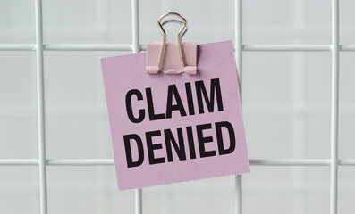 A pink sign that says Claim Denied is hanging on a white metal fence