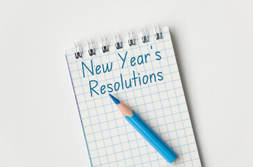 A blue pencil is on a spiral bound notebook with the words New Year's resolutions