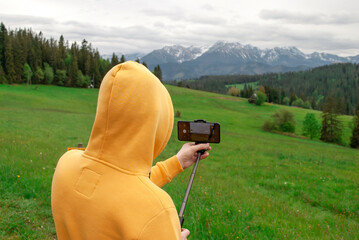 Young guy in a yellow hoodie films a mountain landscape with a camera