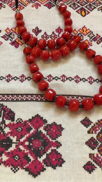 A beautiful Ukrainian embroidered rushnyk covers a table, adorned with vibrant red beads. This traditional composition showcases rich cultural heritage and craftsmanship.