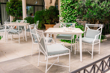 Elegant outdoor cafe terrace with white furniture and lush greenery. Relaxation, summer lifestyle, and modern hospitality.
