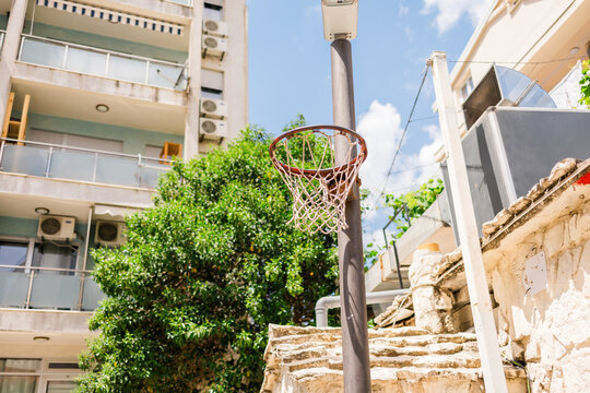 Old basketball hoop in urban courtyard under the summer sky. Concept of street sports, childhood memories, and outdoor recreation in residential neighborhoods.