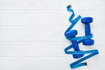 Fitness or healthy lifestyle concept. Blue dumbbells wrapped with blue measuring tape on white wooden background with copy space. Minimal sports accessories idea. Top view with copy space