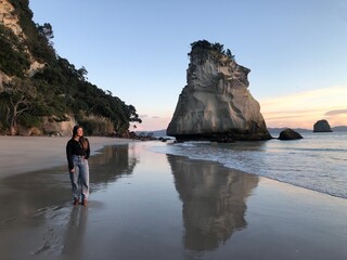 Woman standing on beach with tall boulder (Cathedral Cove New Zealand)