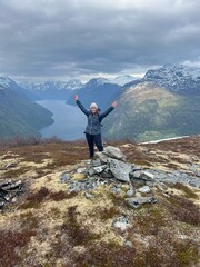 Woman celebrates on top of mountain with view of fjord
