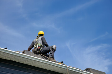 Construction Roofer in Yellow Hard Hat Working on House Roof Edge Against Blue Sky