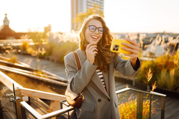 A beautiful woman enjoys the sunset and takes a selfie on her phone. A stylish business woman blogs...