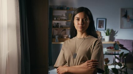Medium portrait of beautiful young biracial female army officer in khaki military t-shirt, with identification tag standing in living room in family home, then looking at camera confidently