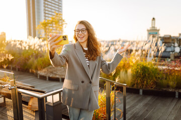 A beautiful woman enjoys the sunset and takes a selfie on her phone. A stylish business woman blogs...