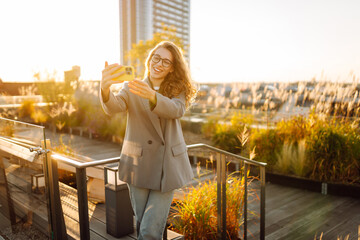 A beautiful woman enjoys the sunset and takes a selfie on her phone. A stylish business woman blogs...