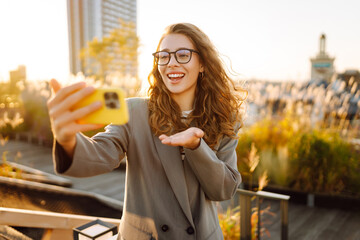 A beautiful woman enjoys the sunset and takes a selfie on her phone. A stylish business woman blogs...