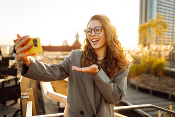 A beautiful woman enjoys the sunset and takes a selfie on her phone. A stylish business woman blogs...