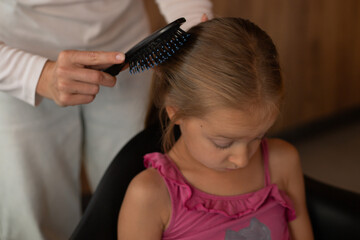 Fototapeta premium female hands combing the hair of a six-year-old girl