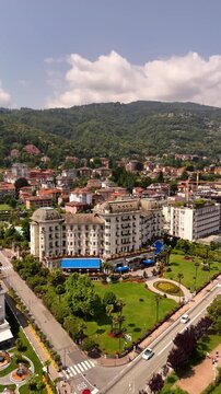 Drone video of Stresa town on Lake Maggiore, Italy, featuring historic grand hotels, bright midday sun, and cars driving along roads near the lake. Vibrant lakeside scene