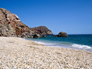Peaceful Greek coastline with sandy beach, bright sky, and steep cliffs in natural sunlight