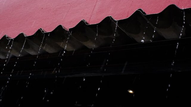 A building with a red roof and a black gutter. The gutter is filled with rainwater, and the rain is falling from the roof. Scene is somber and melancholic