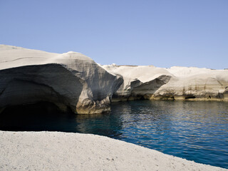 Natural sea caves in white volcanic cliffs at Sarakiniko, Milos island, captured in soft sunlight.