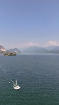 Drone video of a white private yacht sailing across Lake Maggiore from lush Isola Bella, Italy. Elegant luxury journey through iconic Northern Italy&rsquo;s scenic waterscape