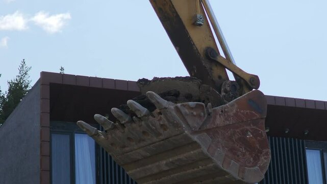 Mechanical digger loading debris into a dumper truck at a construction site, with a modern building in the background