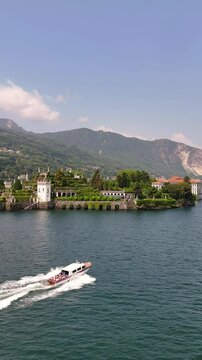 Drone view of a private wooden luxury yacht sailing on Lake Maggiore toward Isola Bella, featuring lush gardens and a majestic baroque palace. Iconic destination for exclusive travel in Northern Italy