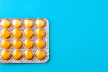 Top-down view of blister pack of yellow cough lozenges or medicine tablets against blue background, flat lay.
