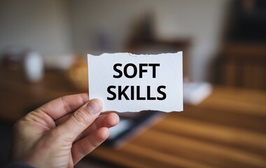 A hand holding a white piece of paper with the text soft skills written on it