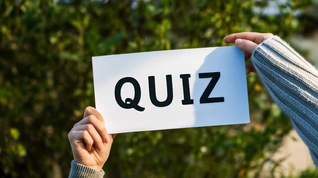 Person holds aloft a simple card with "QUIZ" boldly printed, contrasted against a backdrop of vibrant green leaves, under bright sun light.