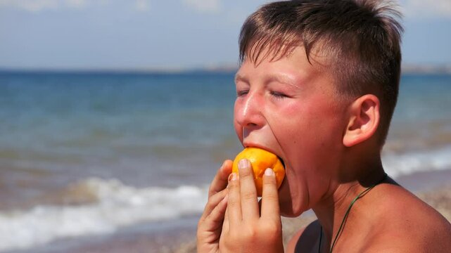 A boy by the sea eats a peach. A light breeze blows over a person. Waves on the sea.