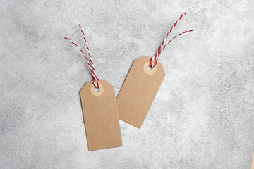 Two blank kraft paper tags with red and white twine loops placed on a textured light gray concrete background, ideal for labeling or gift wrapping themes