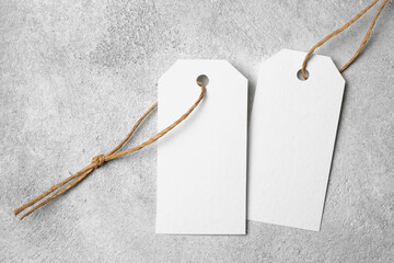 Two white blank paper tags with natural twine placed on a textured concrete surface, perfect for...