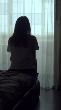 Vertical shot of a woman sitting alone on a bed in an empty room. Her silhouette reflects deep sadness, isolation, and emotional pain. A visual story of depression and mental struggle.