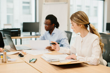 Obraz premium Focused businesswoman reviewing documents in modern office with diverse team