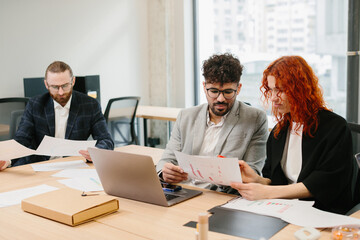 Business people working together in modern office analyzing charts and reports on laptop