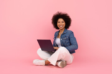 Smiling African American woman with laptop on lap sitting cross-legged on floor, happy black female...