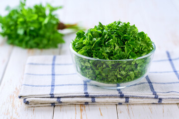 Chopped fresh parsley in a clear glass bowl on a white table, selective focus.
