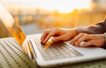 Close-up of young business woman's hands typing on a keyboard in the sunset. Female freelancer...