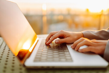 Close-up of young business woman's hands typing on a keyboard in the sunset. Female freelancer...