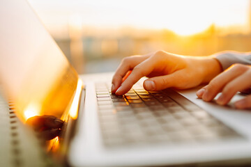Close-up of young business woman's hands typing on a keyboard in the sunset. Female freelancer...