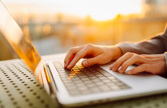 Close-up of young business woman's hands typing on a keyboard in the sunset. Female freelancer working on a laptop and enjoying the sunset. Business concept.