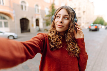 Selfie time! Young woman with headphones taking selfie and blogging while walking through the city...